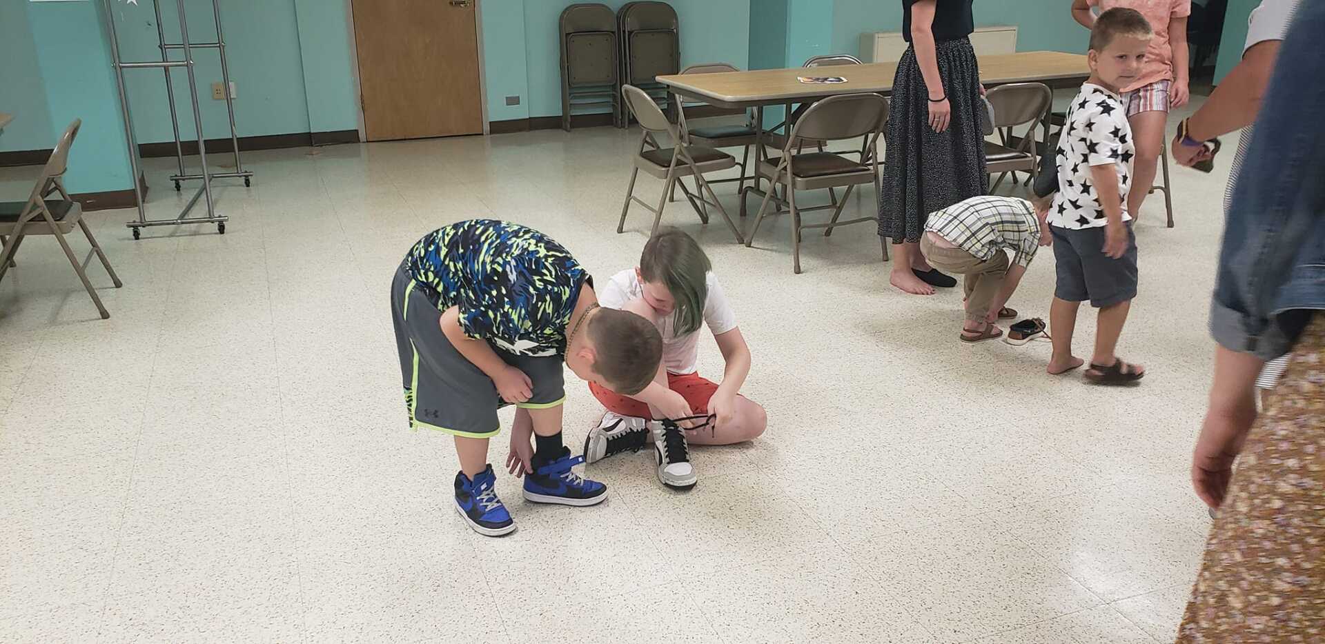 Children crouch around a small toy on a classroom floor while others stand nearby.