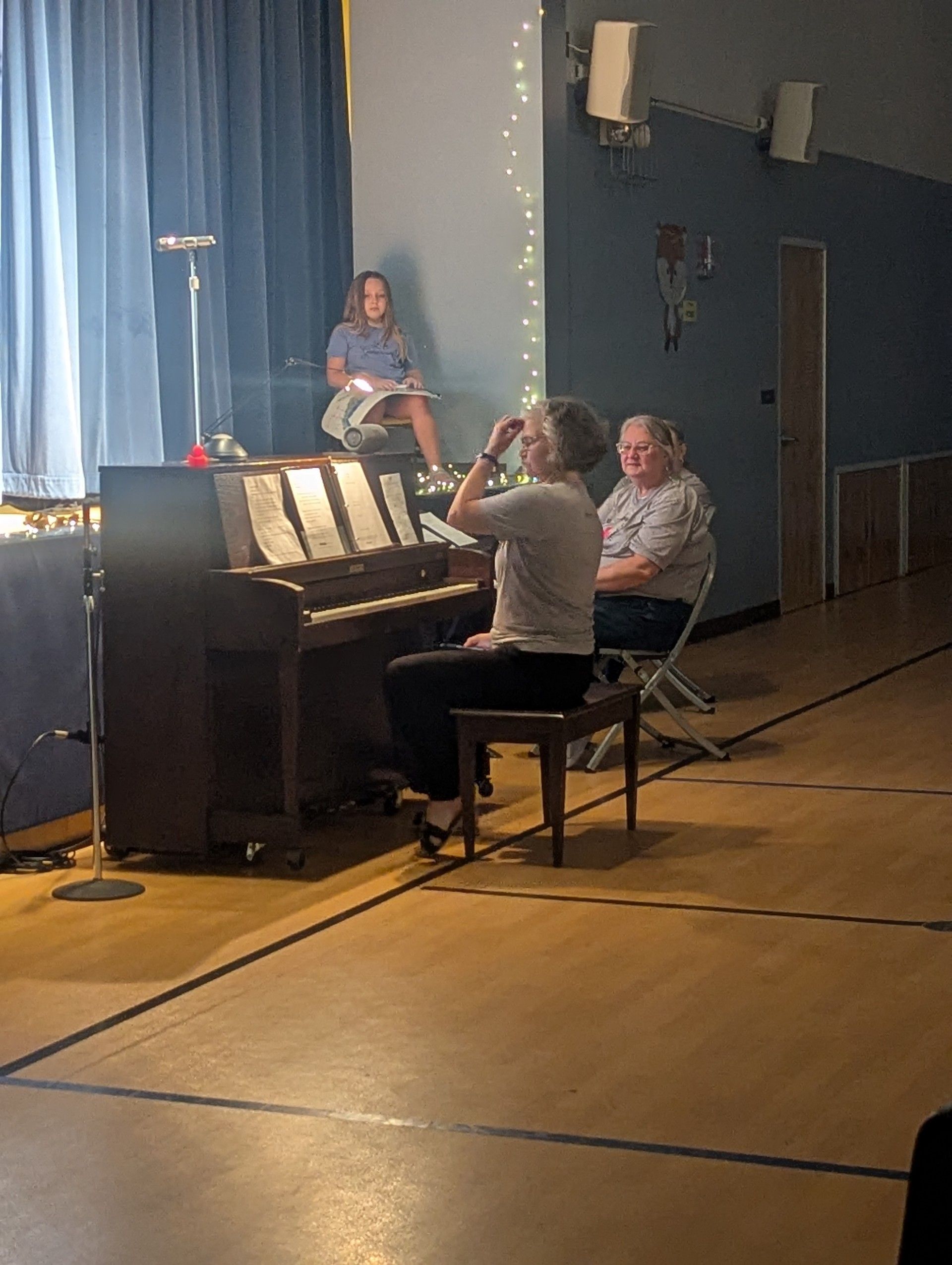 Musicians playing piano and woodwind in a stage rehearsal with blue curtains and microphone stands