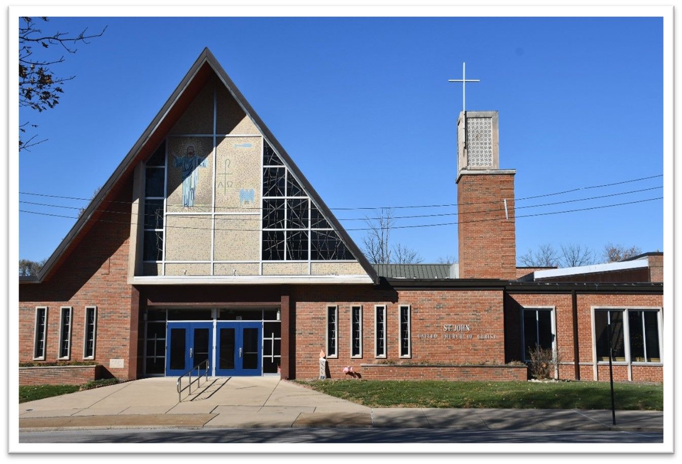 Brick church with a steep triangular roof, blue doors, and a cross on the bell tower against a blue sky
