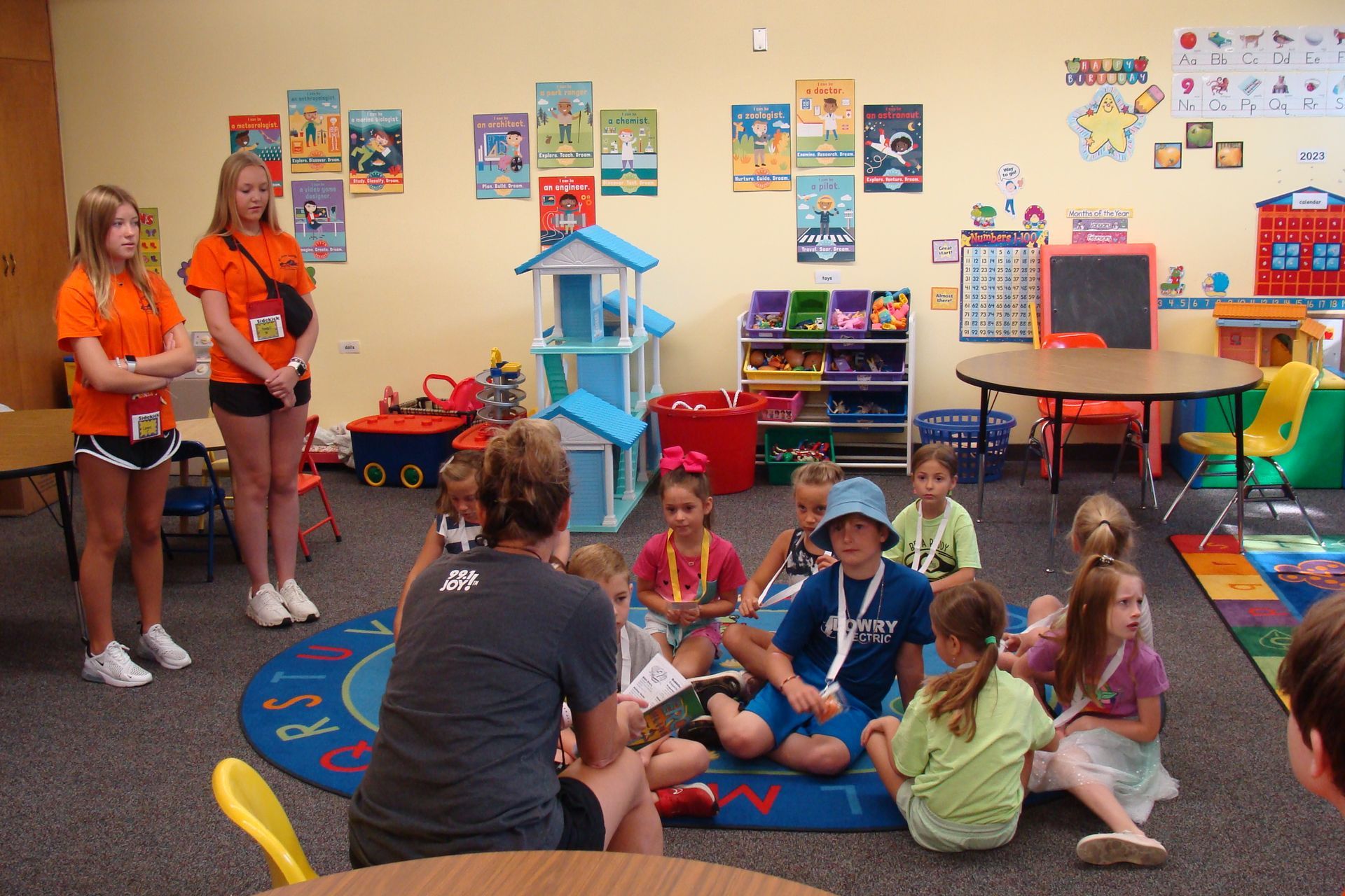 Classroom story time with children seated on a rug, a teacher reading, and colorful books and posters on the walls