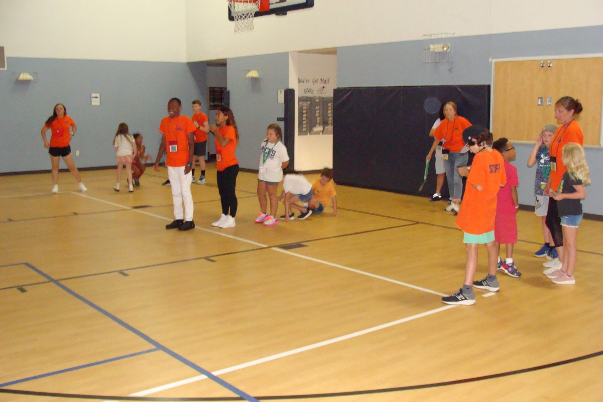 Children in orange and white shirts playing basketball in a gymnasium