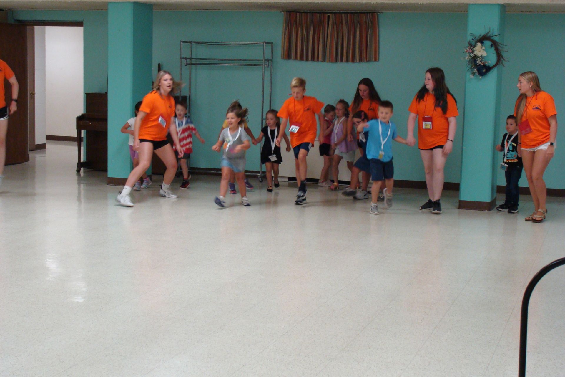 Group of children in orange shirts doing a dance or exercise routine in a room