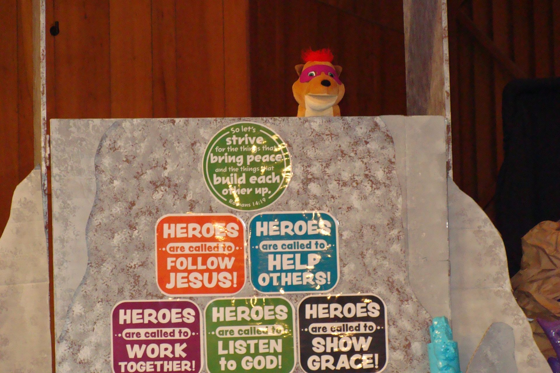 Poster with colorful “Heroes” slogans on a marble surface, topped by a small yellow toy chicken.