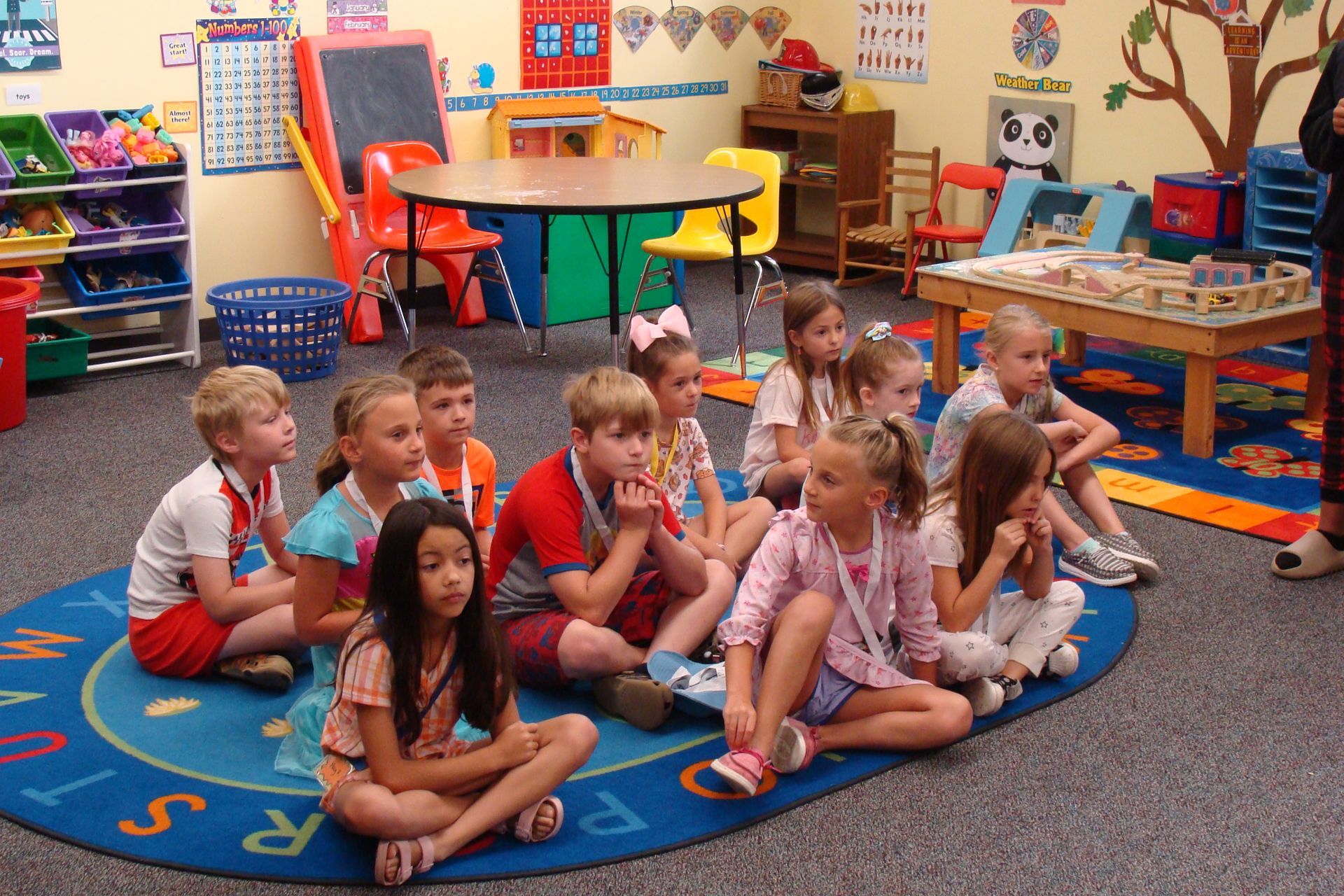 Children sitting cross-legged on a colorful classroom rug during circle time.