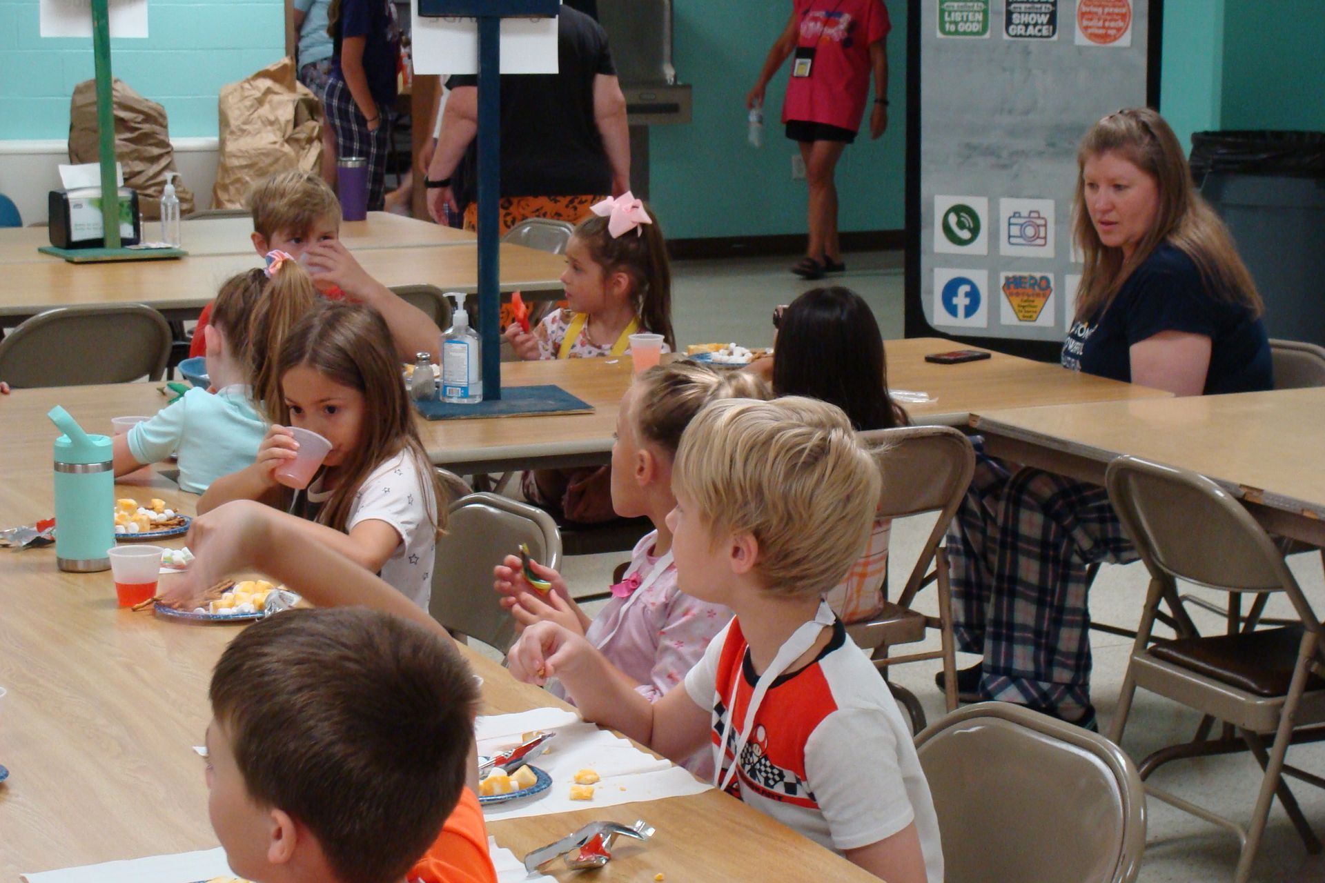 Children seated at a table doing crafts in a bright community room, with an adult nearby.