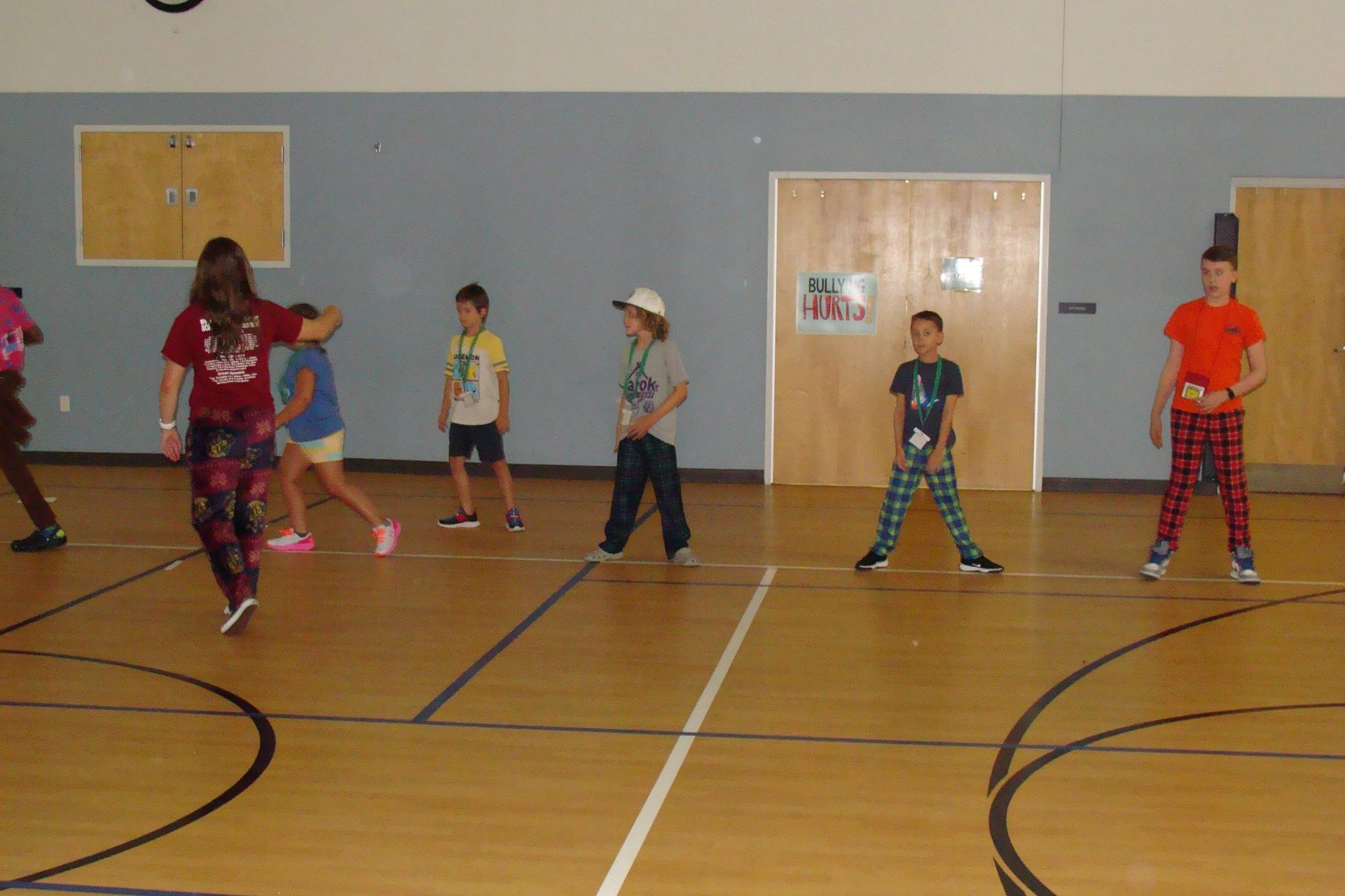 Children practicing dance in a gymnasium, standing in a line on a basketball court.