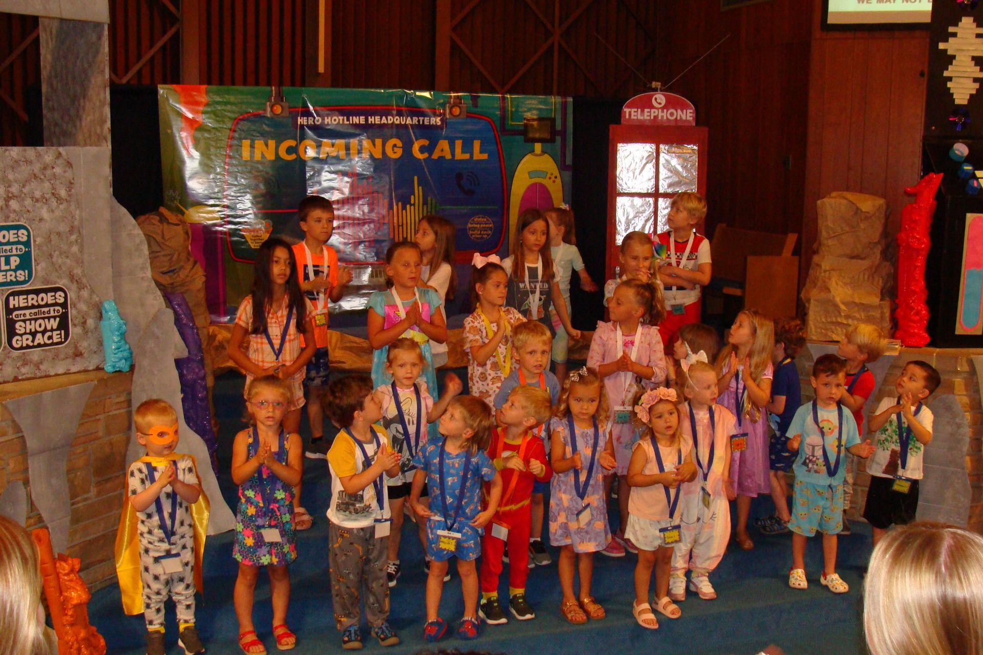 Children in colorful costumes performing on a stage with a circus-themed backdrop