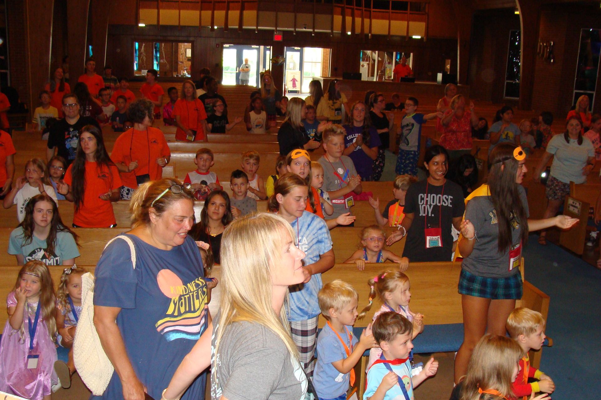 Crowd of people dancing in a hall, with children in front and warm indoor lighting
