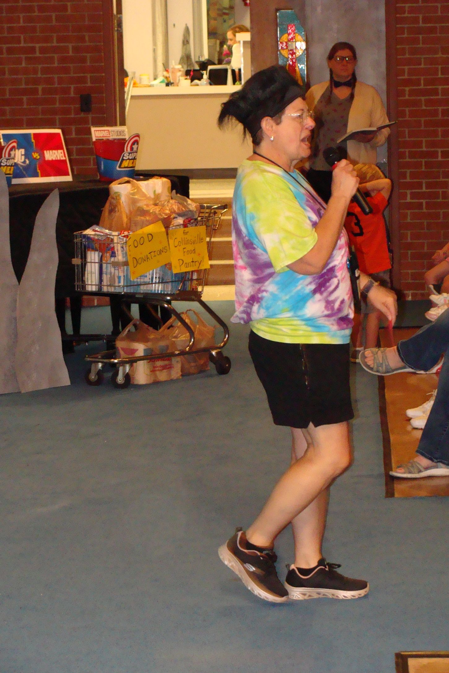 Woman in tie-dye shirt singing into a microphone at an indoor event