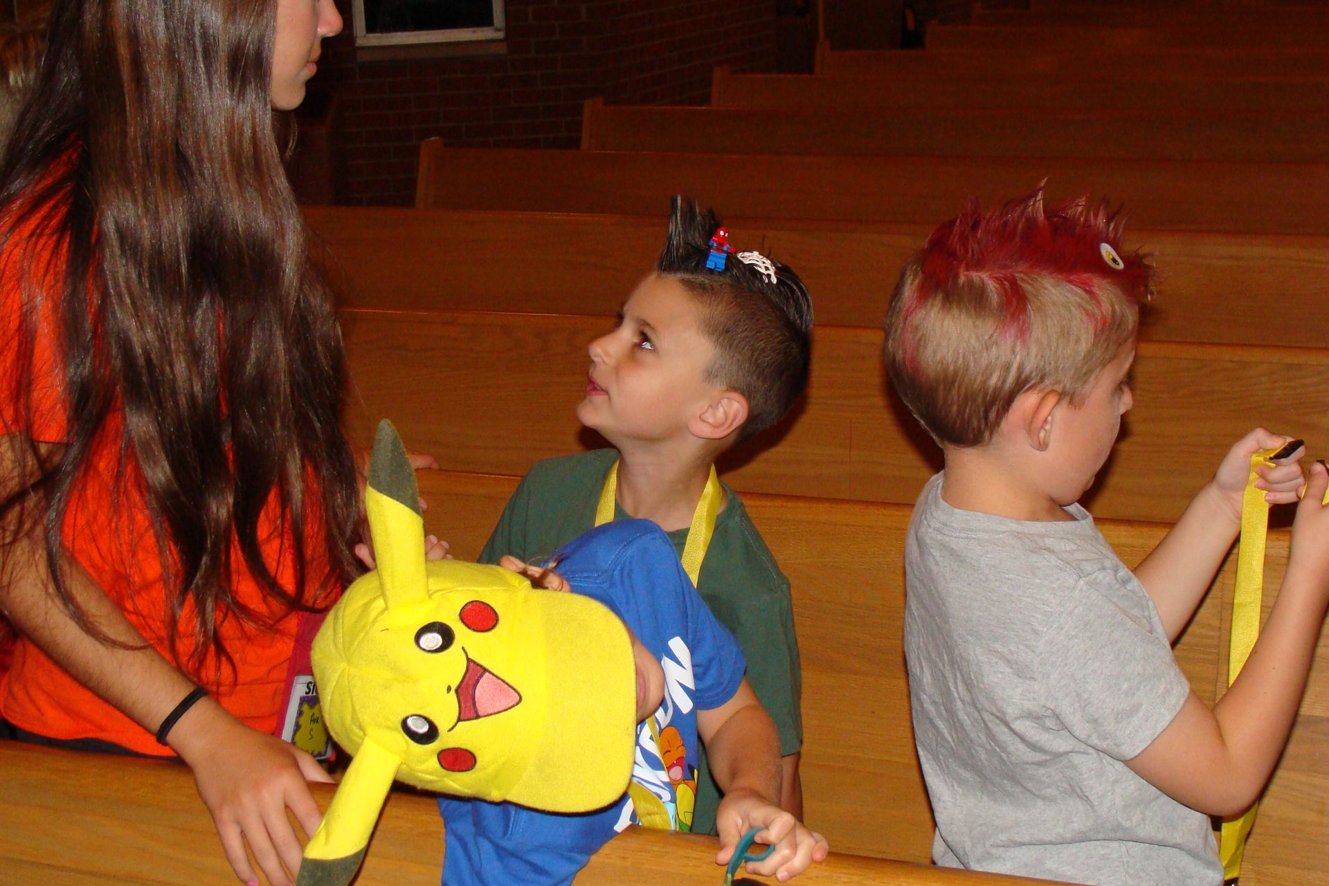 Children sitting in a gymnasium, one holding a Pikachu plush toy