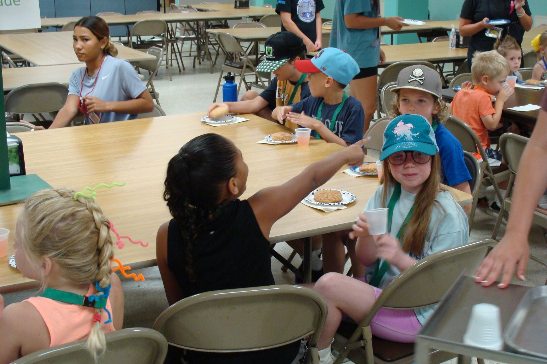 Children seated around a picnic table at a casual outdoor gathering, with plates and cups in front of them.