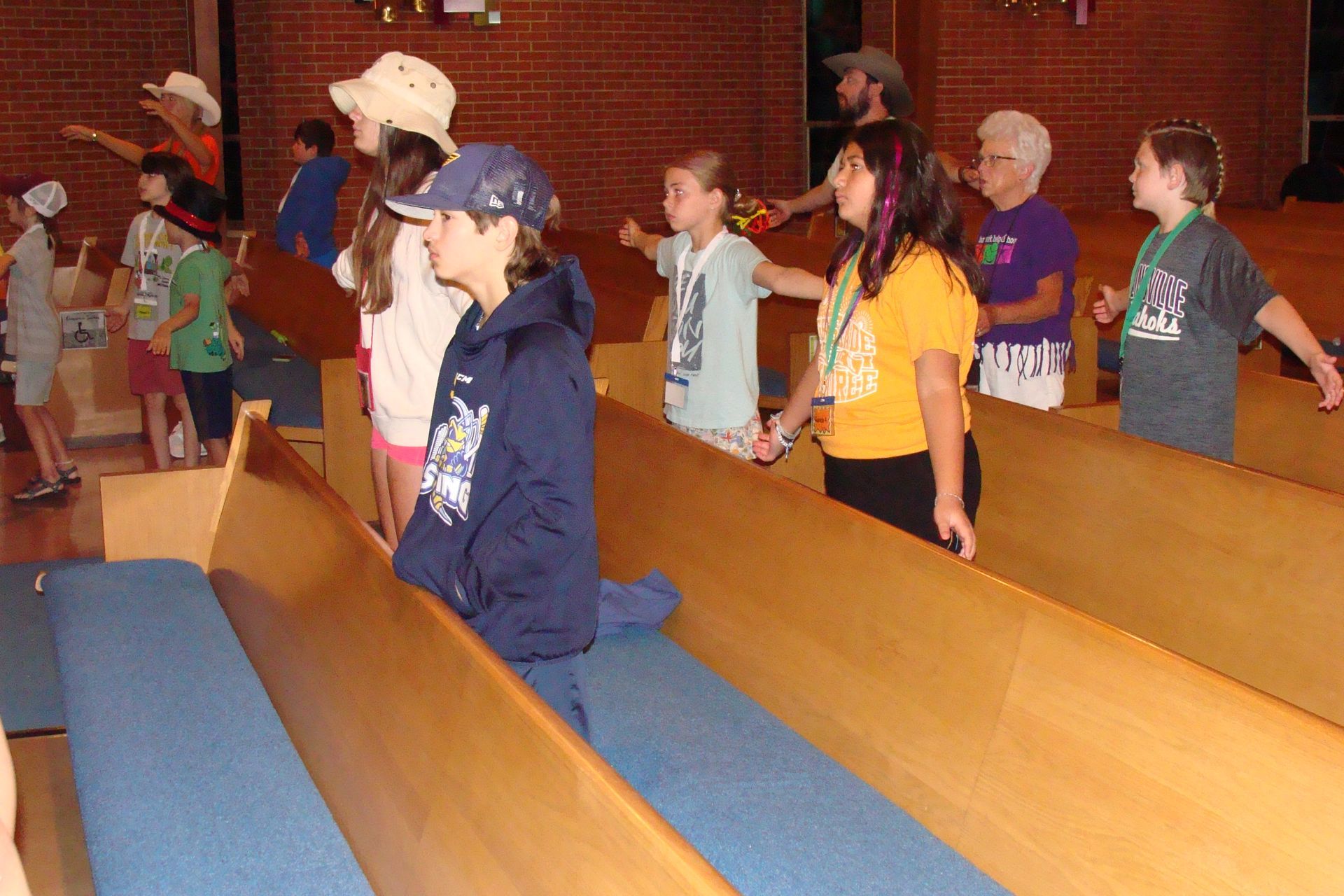 Children standing in wooden church pews during a service, one boy in a blue jacket in the foreground.