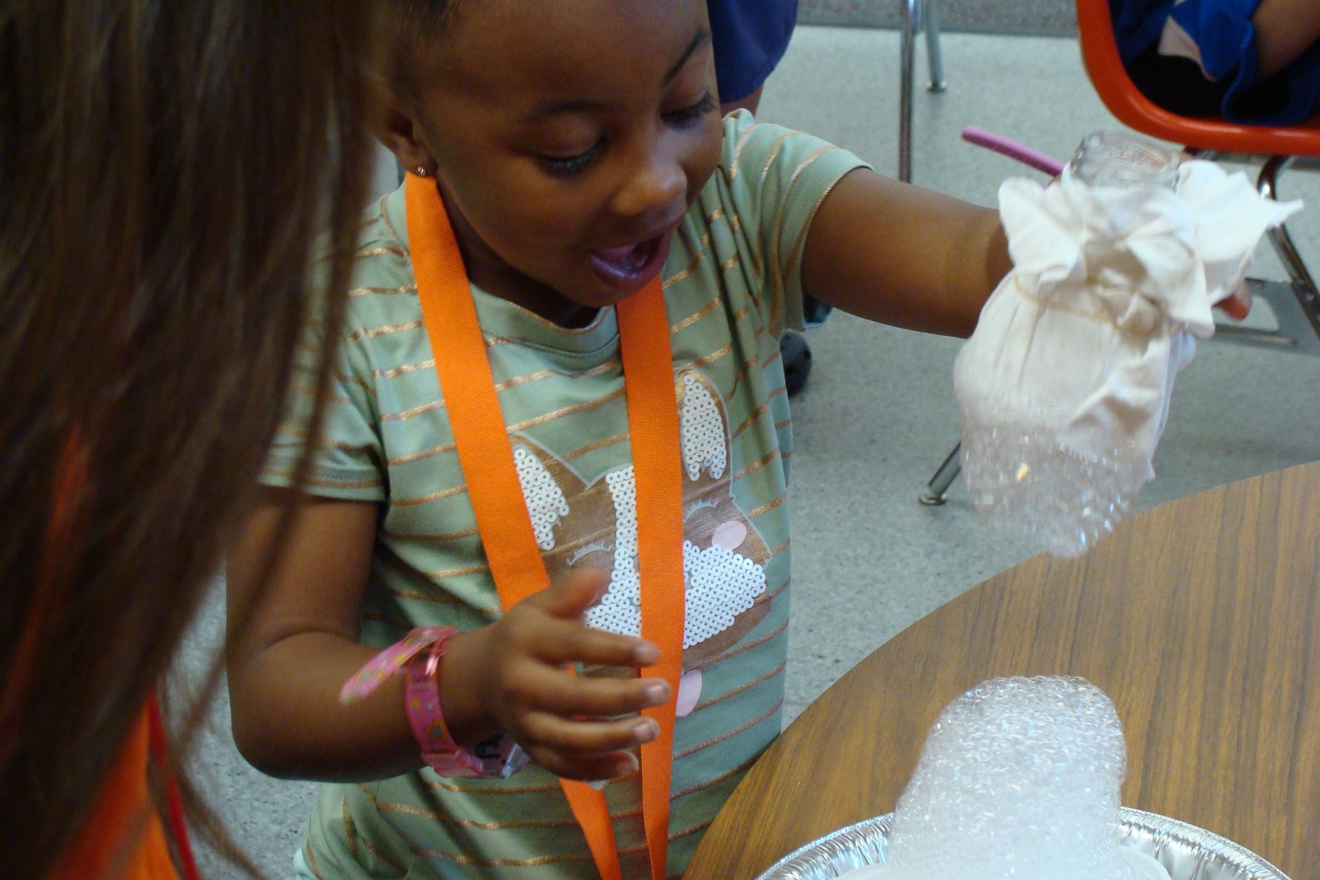 Child at a table holding a clear plastic bag, smiling and examining it during an activity