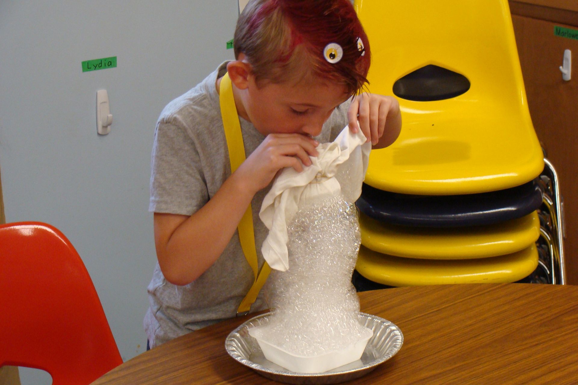 Child pouring foamy white substance into a plate at a table in a classroom area