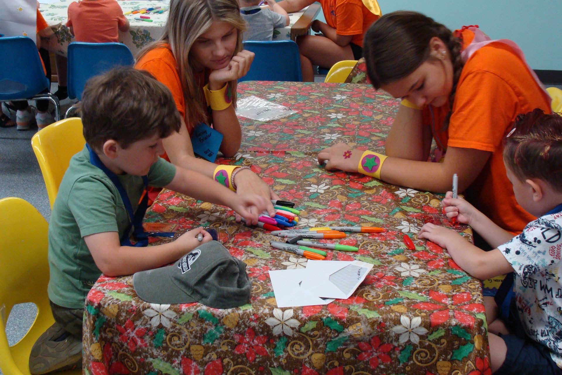 Children at a table making colorful crafts on a floral tablecloth