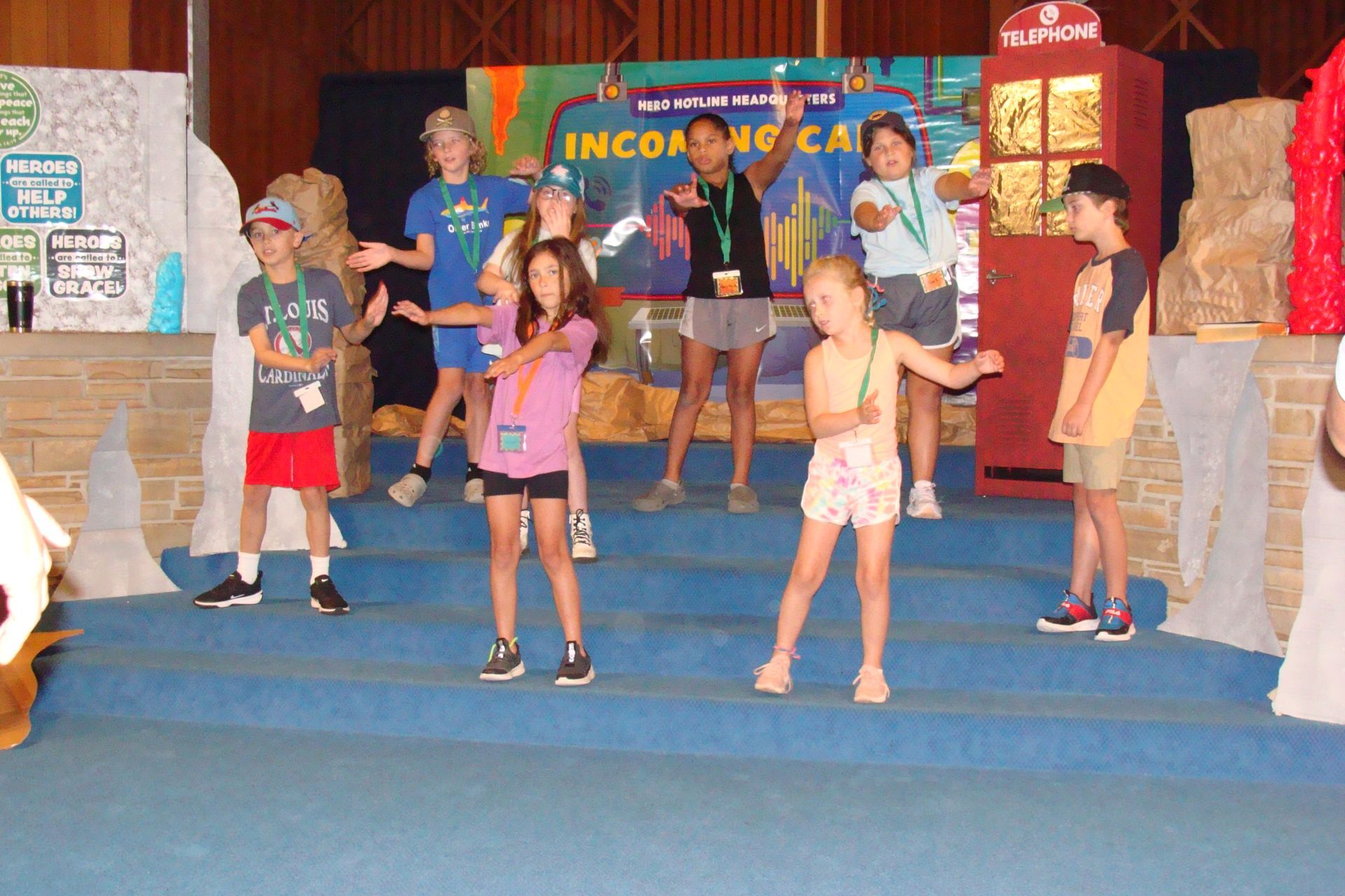 Children posing on stage in front of a colorful “INCOGNITA” backdrop, with balloon decorations nearby