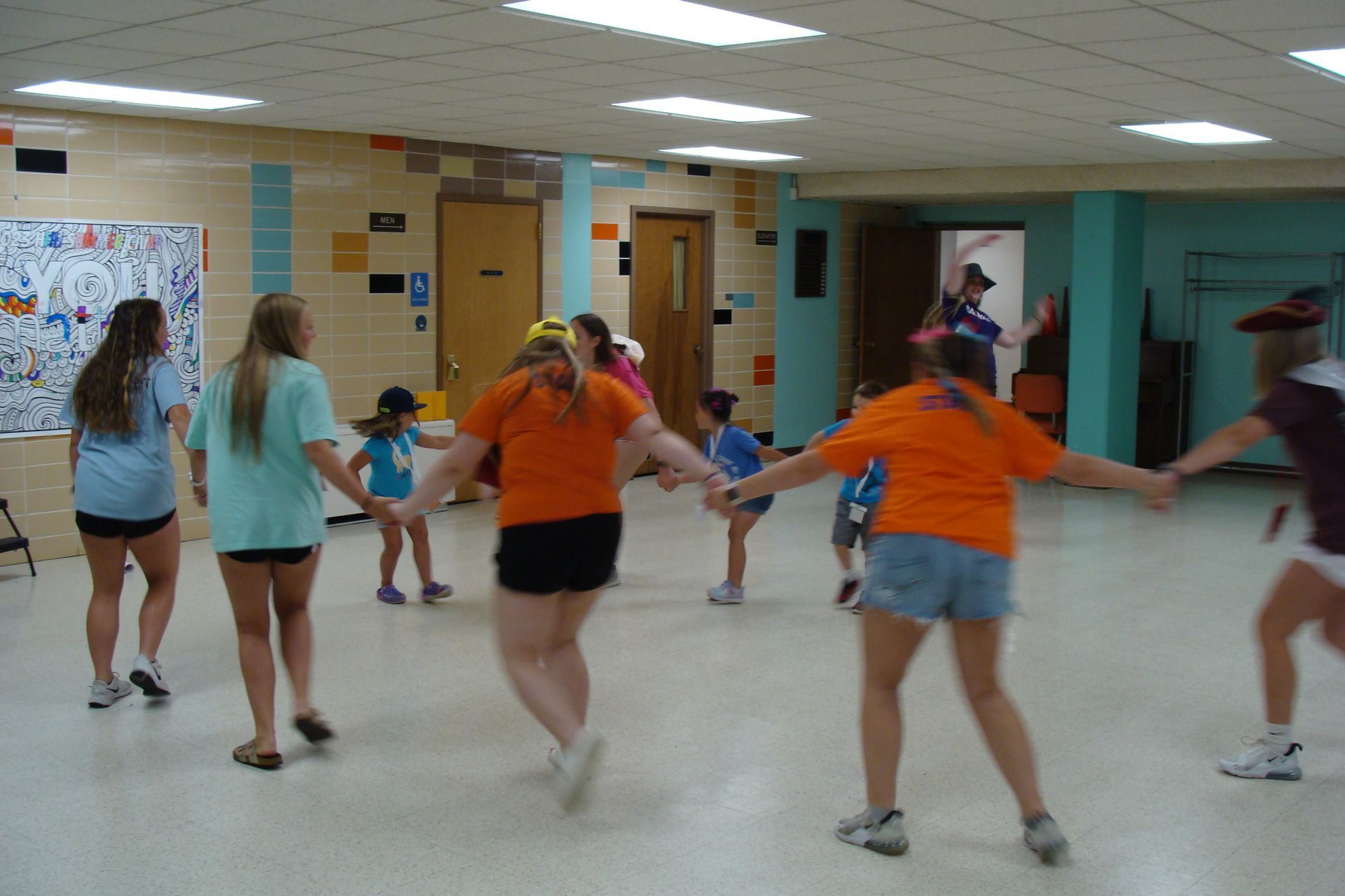 People dancing in a school hallway, with several wearing orange and blue shirts.