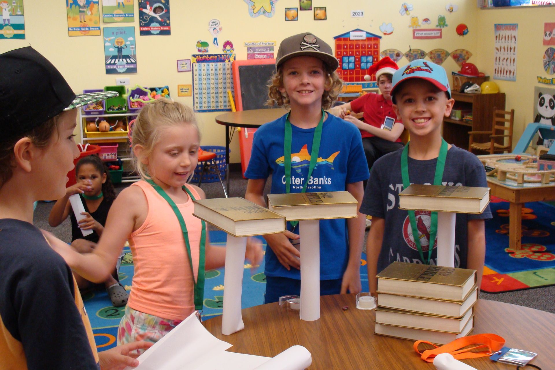 Children in a classroom display handmade tower models on a table