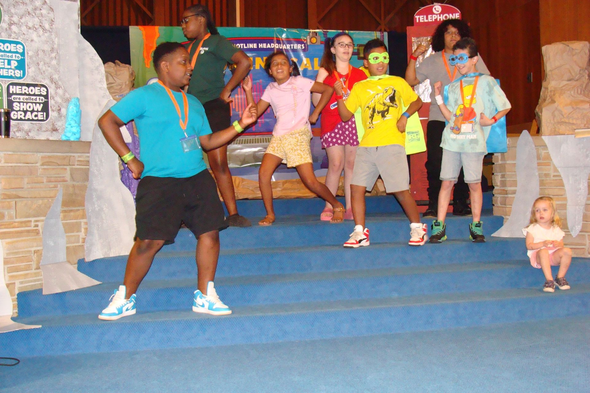 Group of people dancing on blue steps in a colorful indoor space, with a toddler at the right edge