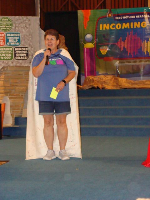 Person speaking into a microphone on a stage with an “Incoming” banner behind them.