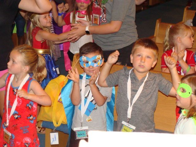 Children in colorful costumes and lanyards at a crowded indoor event