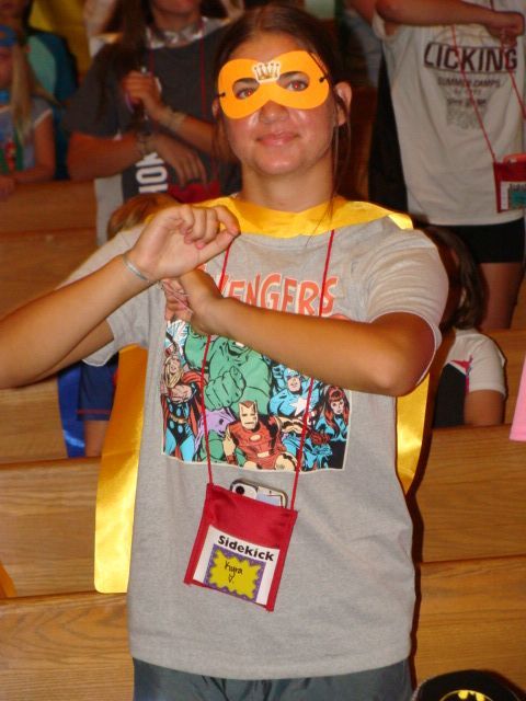 Person in yellow mask and cape posing with crossed arms at a costume event.