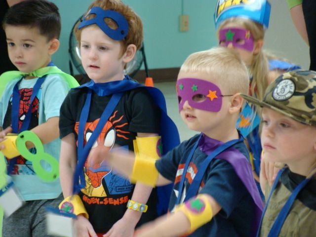 Children in colorful superhero masks and capes standing together at a group event