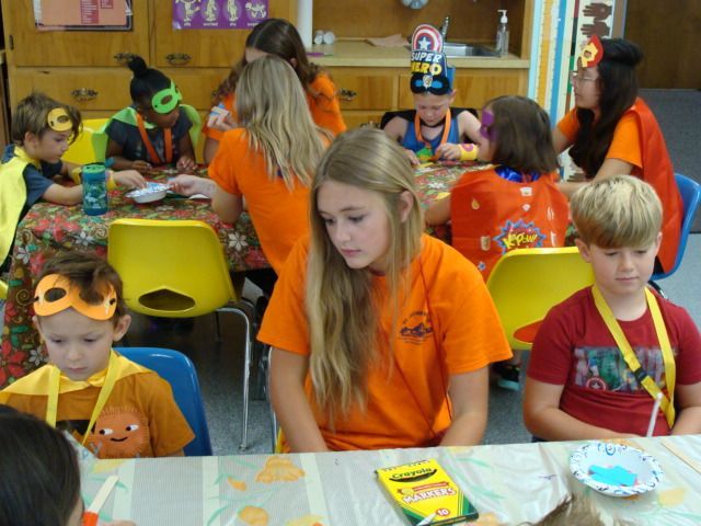 Children in orange shirts seated at tables during a classroom craft activity