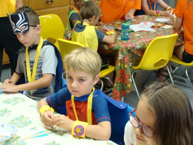 Children seated at a craft table, drawing and coloring with markers in a classroom-like setting