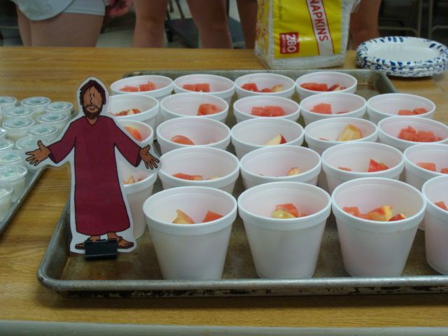 Tray of small white cups with fruit dessert and a paper cutout figure on the left