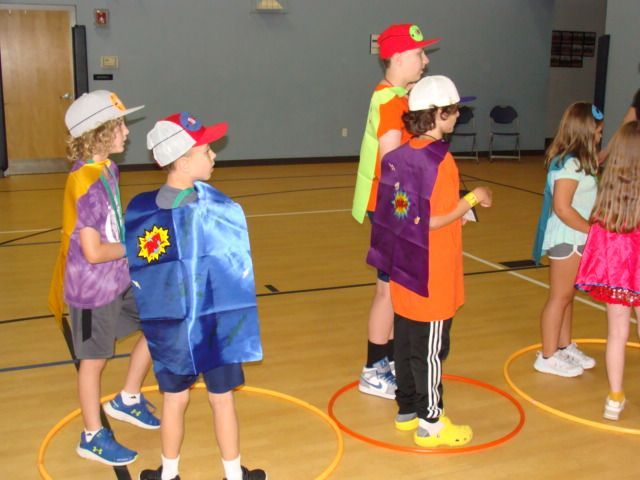 Children in colorful costumes standing in hula hoops on a gym floor