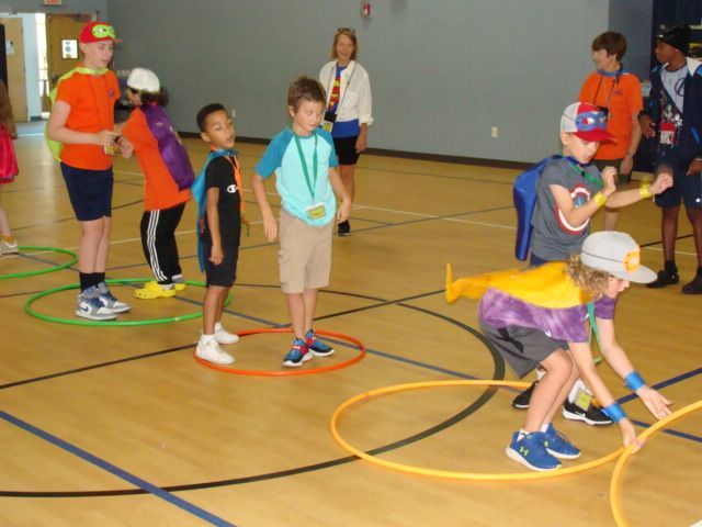 Children playing a beanbag game in a gym, tossing yellow beanbags into hoops on the floor
