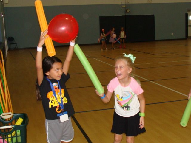 Children in a gym playing with foam sticks and a red ball
