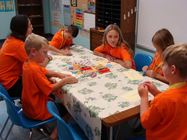 Children in orange shirts playing a board game at a table in a classroom