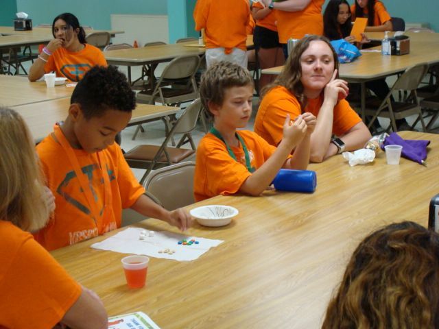 Students in orange shirts doing an activity at tables in a classroom or cafeteria