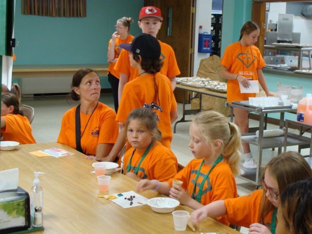 People in orange shirts seated at tables in a community room, eating and talking