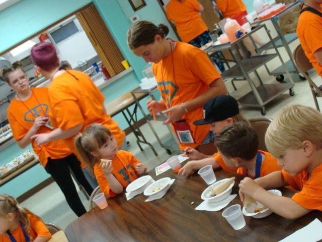 Students in orange shirts eating lunch at a cafeteria table