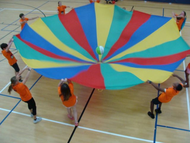 Children holding a large colorful parachute in a gymnasium during group play