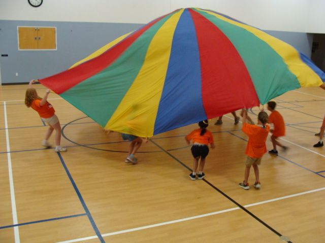 Children lifting a colorful parachute in a gymnasium during a group activity