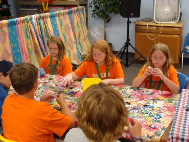 Children in orange shirts sit around a table playing a colorful card game.