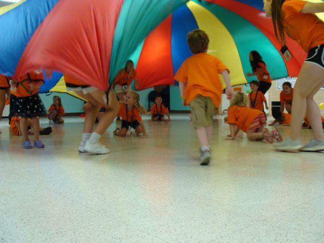 Children under a colorful parachute canopy at an indoor play activity