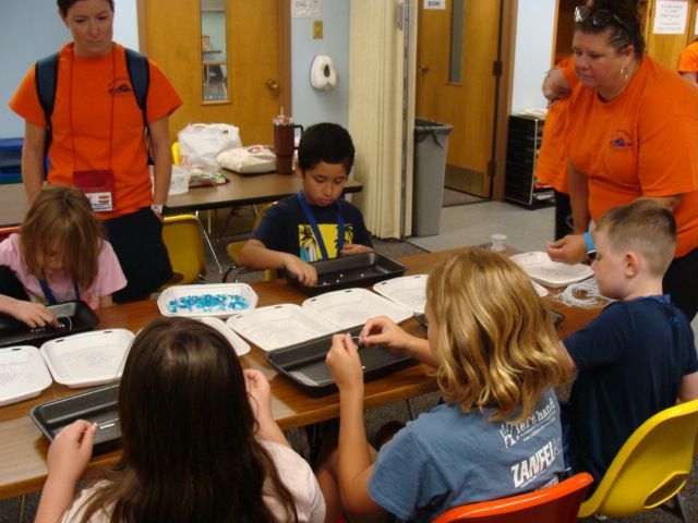 Students working at desks in a classroom with two teachers standing nearby