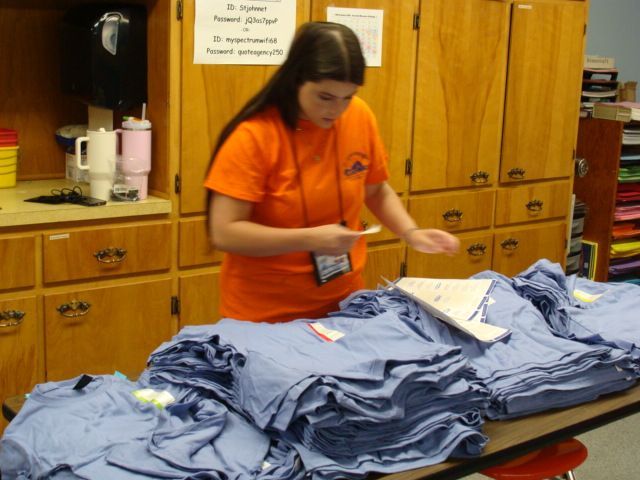 Person in orange shirt folding blue clothes on a table in a laundry room.
