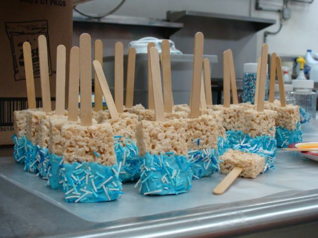 Tray of blue-wrapped rice crispy pops with wooden sticks on a kitchen counter