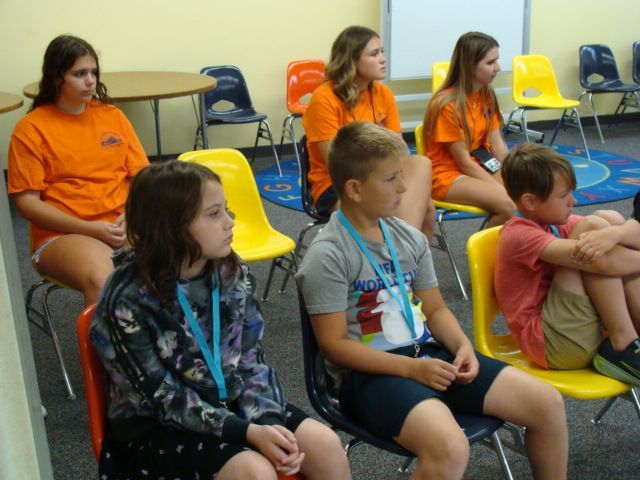 People seated on colorful chairs in a classroom, listening attentively.