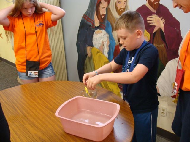 Children doing a classroom activity with a pink tub on a table, one stirring inside it