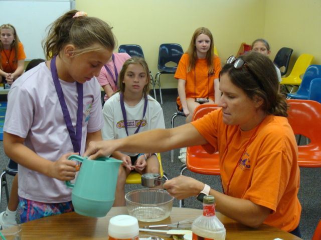 Adult and children pouring liquid into a container at a table in a classroom