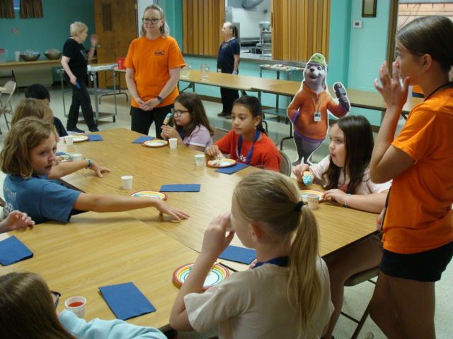 Children and adults gathered around a table in a classroom, doing a hands-on craft activity.