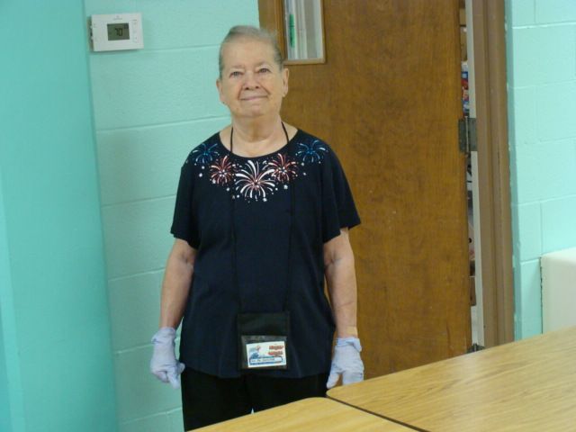 Person standing in a hallway beside a wooden door, wearing a black shirt and gloves.