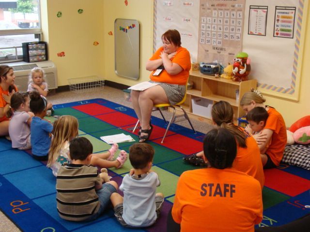 Teacher reading to seated children in a colorful classroom circle time.